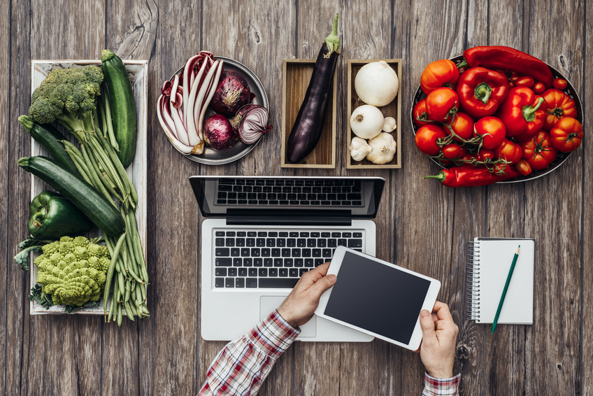 Green, red, purple, white vegetables on a rustic kitchen worktop and hands using a digital tablet, healthy eating and technology concept, flat lay