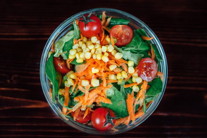 Bunter Salat mit Spinat, Karotten, Mais und Tomaten in einer Glasschüssel